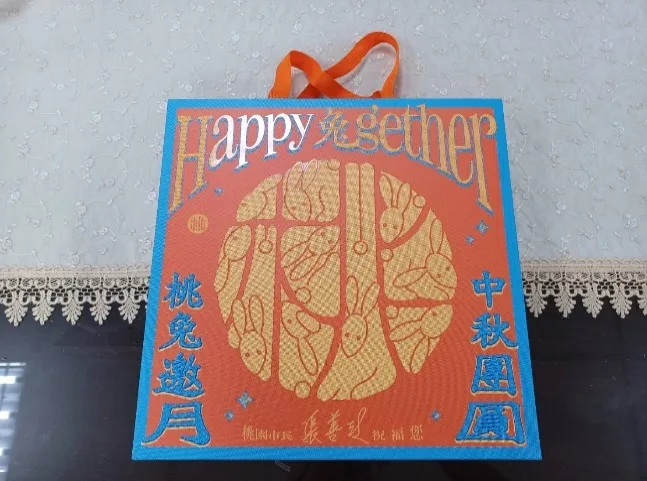 橘色不織布手提袋，正面以金色印滿兔子圖樣，寫著「Happy兔gether」「桃兔邀月」「中秋團圓」