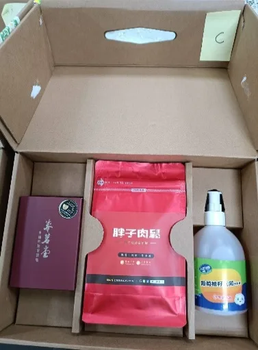 打開的牛皮紙禮盒俯拍，盒蓋貼有黃色標籤「C」，盒內放著一盒紅玉茶、一包紅色包裝肉鬆與一瓶洗手液