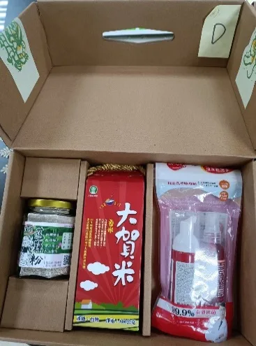 打開的牛皮紙禮盒俯拍，盒蓋貼有黃色標籤「D」，盒內放著一罐蓮藕粉、一盒大賀香米與一組抗菌洗手隨身瓶