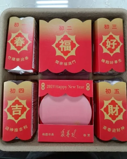 打開的禮盒俯拍，盒內排列五個紅金相間的長條紙盒，分別標示初一到初五，中央為粉紅色圓形皂片