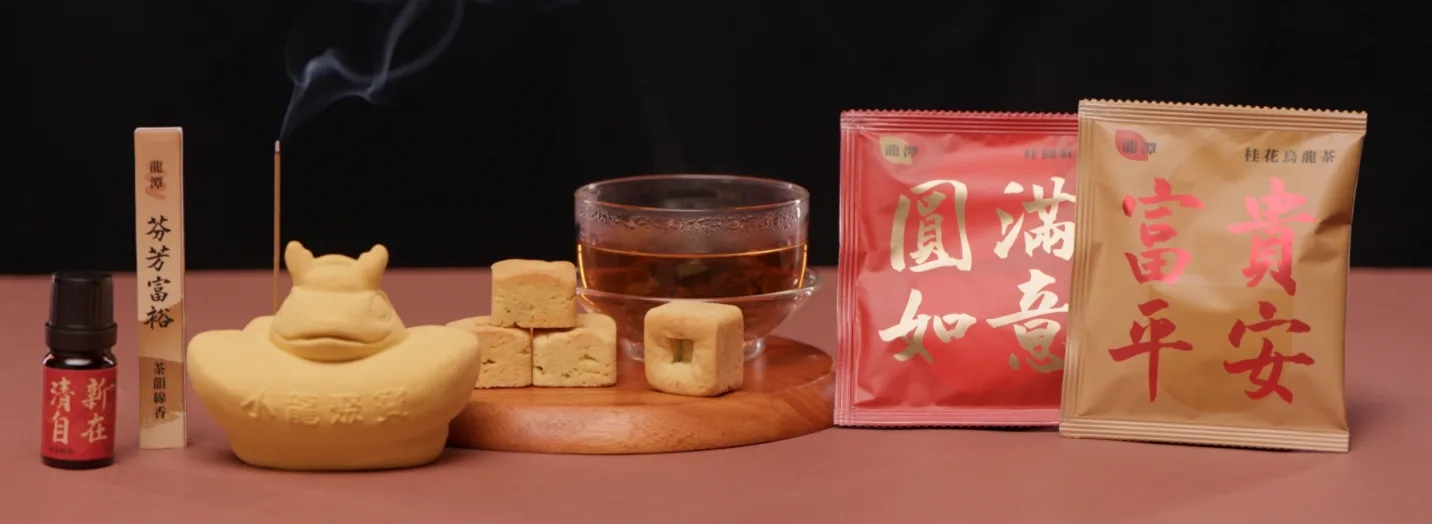 情境擺拍：由左至右為精油瓶、線香座與燃著的線香、元寶造型香氛座、茶湯與方塊酥、兩包紅色與金色茶包