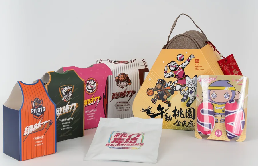 四個球衣造型的紙盒並排，右側為粽形禮盒與吉祥物造型包裝，前方放著一包白色毛巾